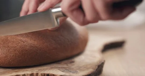 Slide shot of young female hands slicing rye wheat rustic bread on cutting board Stock Footage