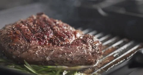 Slide slow motion shot of cooking rib eye steak with herbs on grill pan Stock Footage 76034074
