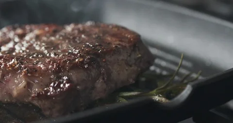 Slide slow motion shot of cooking rib eye steak with herbs on grill pan Stock Footage 99831200