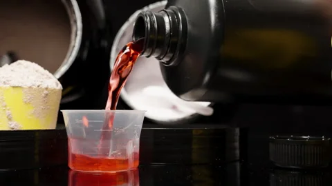 Slider Shot Across a Black Table as Red Sports Supplement Is Poured, with Stock Footage 277471237