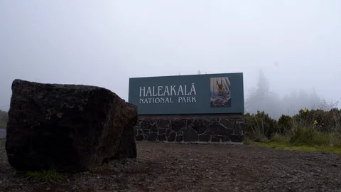 Slider shot boulder in foreground and foggy Haleakala National Park sign Maui Stock Footage 118999850