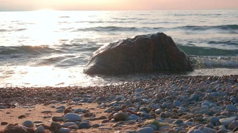 Slider Shot of Small Waves Breaking Over Colorful Boulder Along Beach at Sunset Stock Footage 186595294