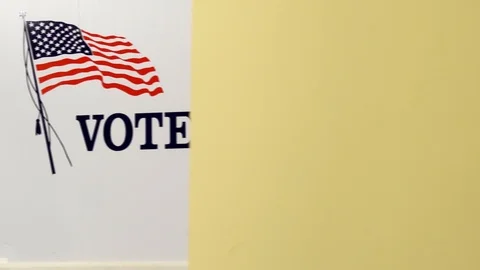 A slider shot from yellow wall to voting booths in front of a large America flag Stock Footage 125541237