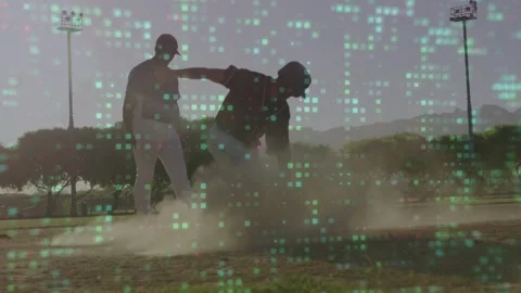 Sliding player reaching baseball base feet-first, kicking dust, teammate aiding Stock Footage 333318194