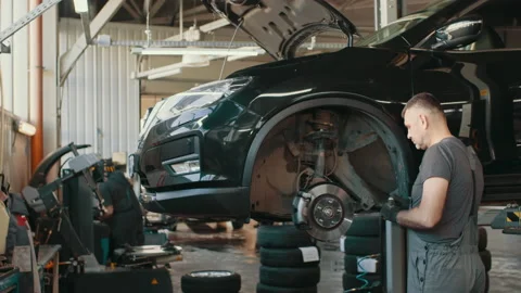Sliding shot of auto mechanic checking SUV suspension of a lifted car Stock Footage 180958657