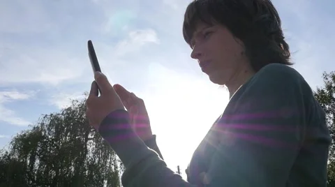 Sliding typing smart phone touchscreen woman stay against the sun slow motion Stock Footage 64072528