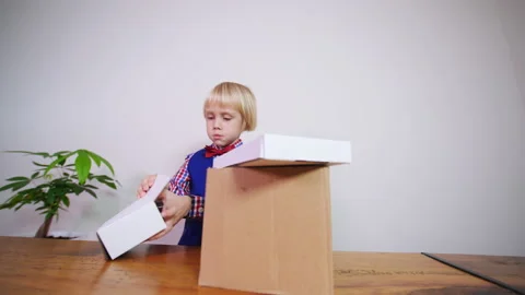 Sliding view of a caucasian boy dressed like a postman opening parcels Stockbeeldmateriaal 229619656