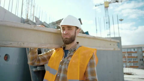 Sliding view of worker carrying long heavy beam. A man's look at the camera Stock Footage 241167928