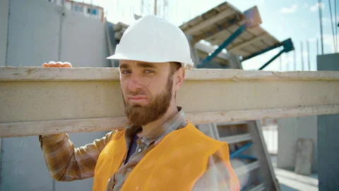Sliding view of worker carrying long heavy beam. A man's look at the camera Stock Footage 247768664