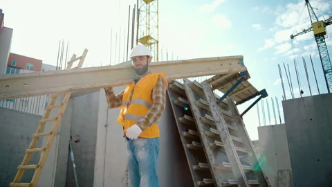 Sliding view of worker carrying long heavy beam. Frame house site building Stock Footage 258670777
