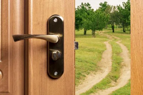 A slightly open door behind which is a country road leading to a pine forest. Stock Photos