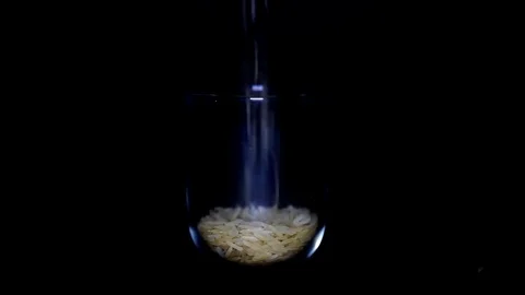 Slim and lengthy raw long grain rice in transparent glass on black background 스톡 동영상 75892474