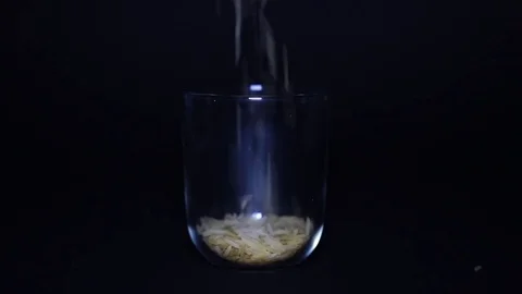 Slim and lengthy raw long grain rice in transparent glass on black background 스톡 동영상 75892475