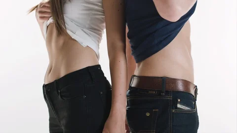 A slim couple stands back to back holding up their shirts to show their Stock Footage 128621195
