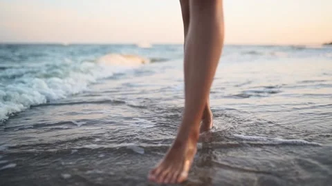 Slim female legs and feet walking along sea water waves on sandy beach. Pretty Stock Footage