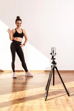 Slim female recording tutorial video for fitness vlog, waving hand, saying hi to Foto stock