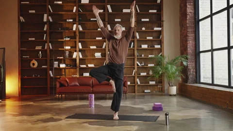 Slim man in his 50s performing tree pose on a fitness mat, yoga exercise Stock Footage 340902030