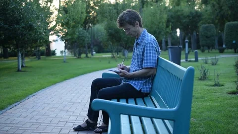 Slim man sits on a bench and writes in notepad Stock Footage 71218293