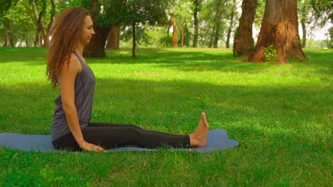 Slim woman does forward bend pose in park Stock Footage 98496084