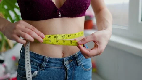 Slim young woman measuring her thin waist with a tape measure, close up  Stock Photo