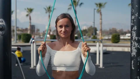 Slim young woman training pull ups with resistance band in outdoors at sunny Vídeos de archivo 234013946