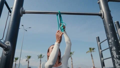 Slim young woman training pull ups with resistance band in outdoors at sunny Video stock 234014064
