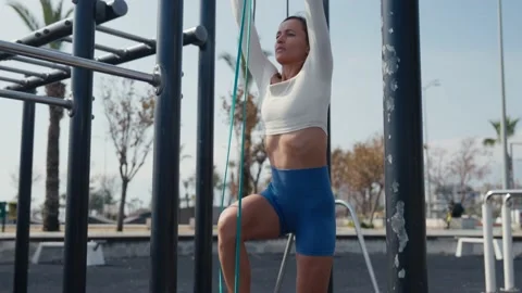 Slim young woman training pull ups with resistance band in outdoors at sunny Vídeos de archivo 234014105