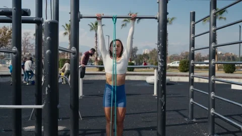 Slim young woman training pull ups with resistance band in outdoors at sunny Stock Footage 234014156