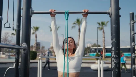 Slim young woman training pull ups with resistance band in outdoors at sunny 스톡 동영상 234014170