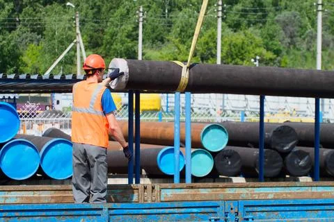 Slinger in hard hat and high-visibility vest unloads metal pipes for Foto stock