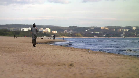 SloMo: Man with Beard in Protective Face Mask Running by the Beach at Dusk - Stock Footage 130736308