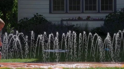 Slomo of a toddler running through a sprinkle in summer Stock Footage 76709617