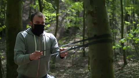 SloMo: Young Bearded Man in Face Mask Exercising with Resistance Bands in Lush Stock Footage 130780684