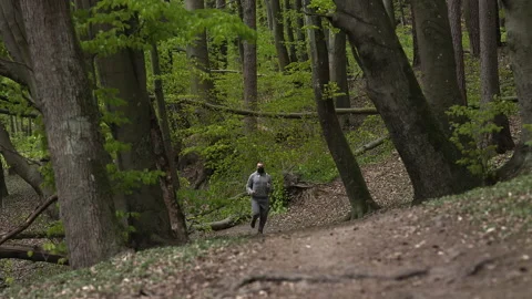 SloMo: Young Man with Beard in Face Mask in Sportswear Running in a Lush Forest Stock Footage 130780237