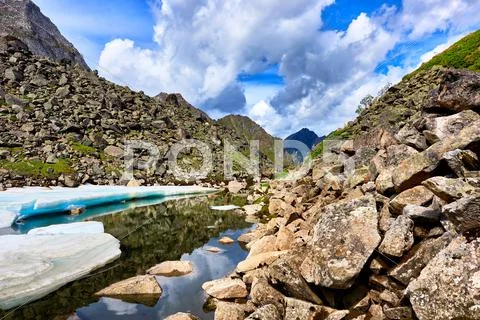 Slope of boulders at the water with pieces of ice melting Siberian summer . E Stock Photos