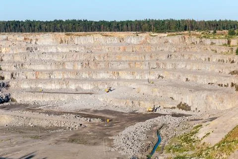 Slope of operating granite quarry with mining equipment on ledges Stock Photos