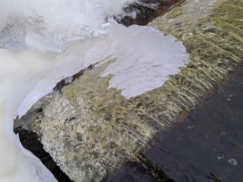 Slope of a waterfall in early spring that flows under a canopy of ice Stock Photos