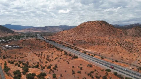 Slow advancing flight over dual carriageway with trucks revealing vast arid red Stock Footage 336499795