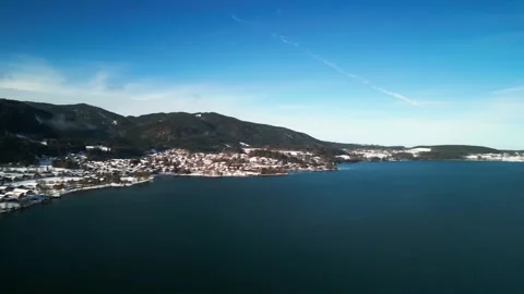 Slow aerial pan over alpine lake amidst snowy mountains and small mountain towns Stock Footage 272622014