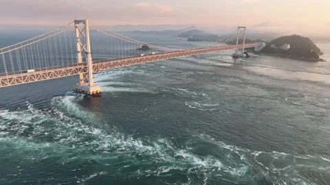 Slow aerial pullback and rise over strong current under bridge at sunset Stock Footage 200036970