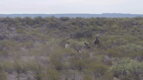 Slow aerial push over western landscape, ranchers riding horses off into Stock Footage