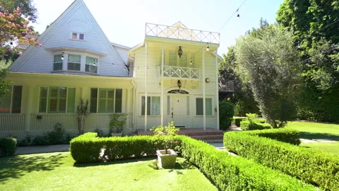 Slow approach to a white two story farmhouse with formal hedge garden Stock Footage 345679960