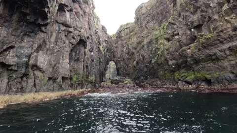 Slow boat POV drifting in front of a majestic natural sea arch, Faroe Islands Stock Footage 339270997