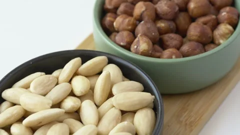 Slow camera movement passes over bowls of almonds, hazelnuts and pecans showing 库存影片 345652458