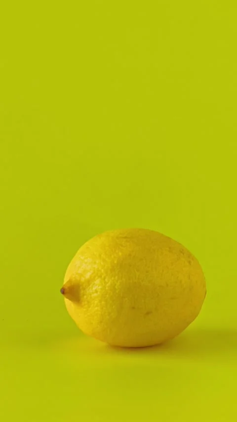 Slow camera push-in on a fresh, whole lemon on a vibrant yellow background. Video stock 338182360