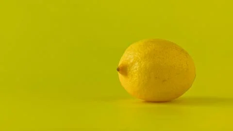 Slow camera push-in on a fresh, whole lemon on a vibrant yellow background. Stock Photos