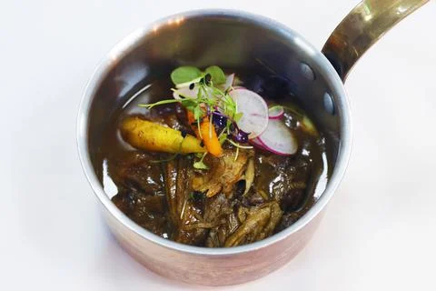 Slow cooked pulled lamb shoulder in a coper pot with baby carrots and slice r Stock Photos