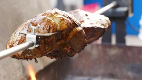 Slow cooking a large piece of meat on a rotating spit over open fire in backyard 스톡 동영상 332053836