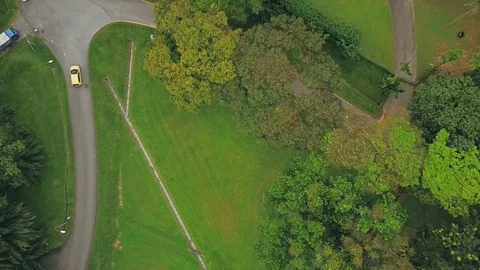 Slow descending top-down shot of a yellow car driving along a pavement in a park Stock Footage 108801829