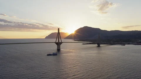 Slow drone pan of Rio-Antirrio Bridge silhouette at sunset with ferry crossing Stock Footage 341933997
